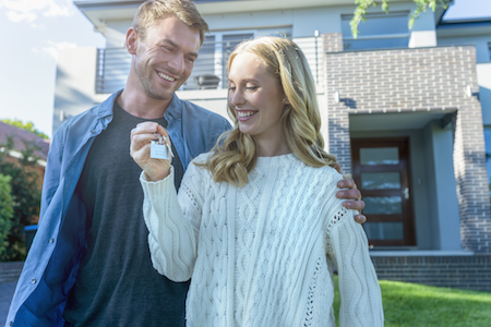 Jeune couple avec clé en main devant la nouvelle maison qu'ils ont achetée